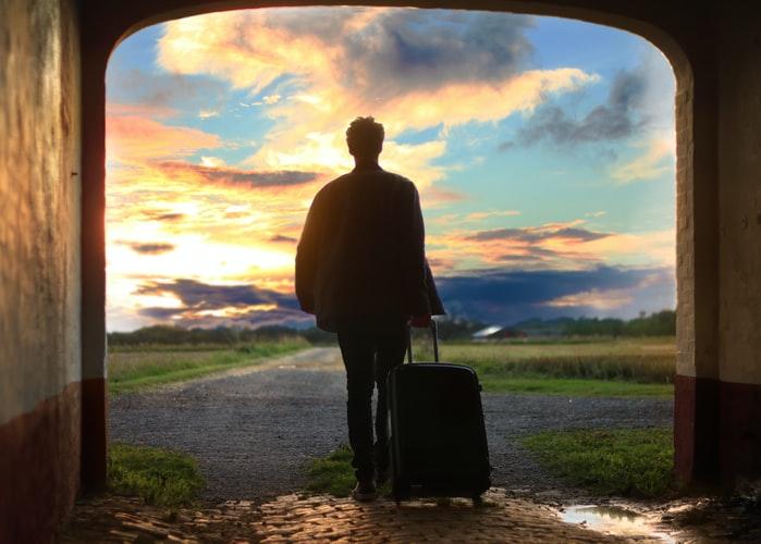 Man with suitcase walking toward sunset