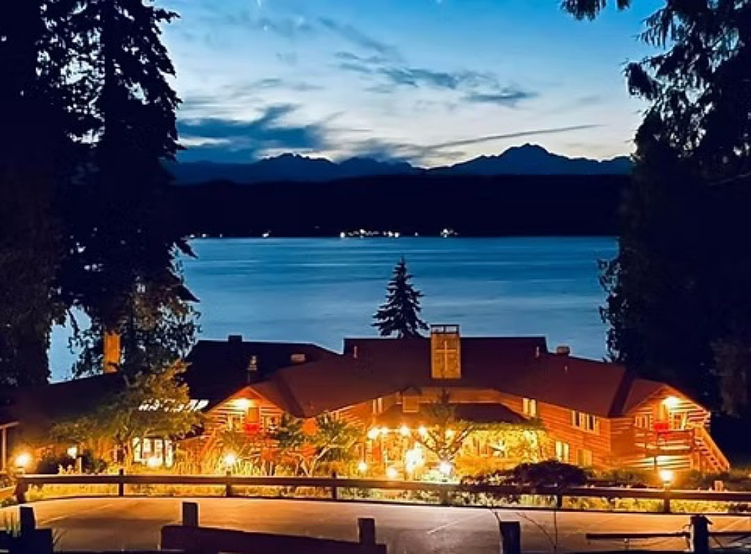 Large house on the edge of a lake with mountains in the background at dusk.