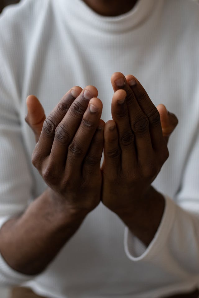 man praying in a turtleneck with only a view of his hands in prayer