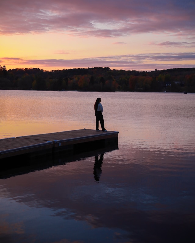 person on the edge of a dock looking into the distance at sunset